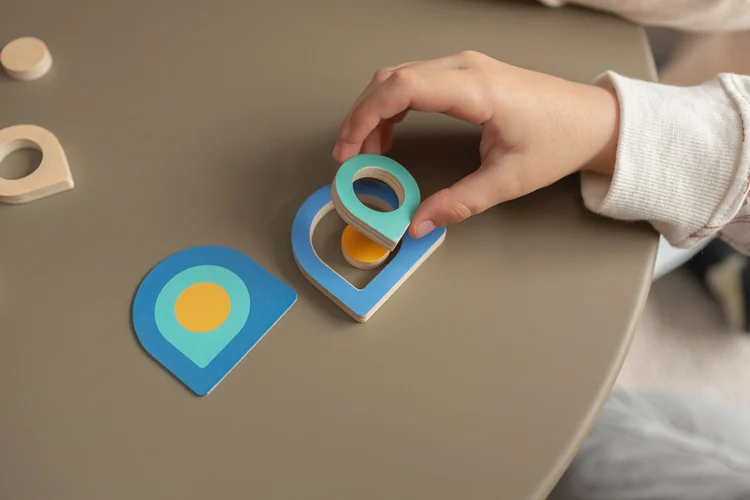Dłonie dziecka układają trzy kolorowe kształty w grze 3 Shape Memo BS Toys