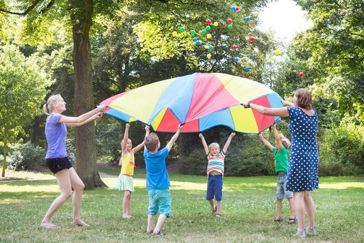 Dzieci unoszą kolorową chustę animacyjną BS Toys na trawie